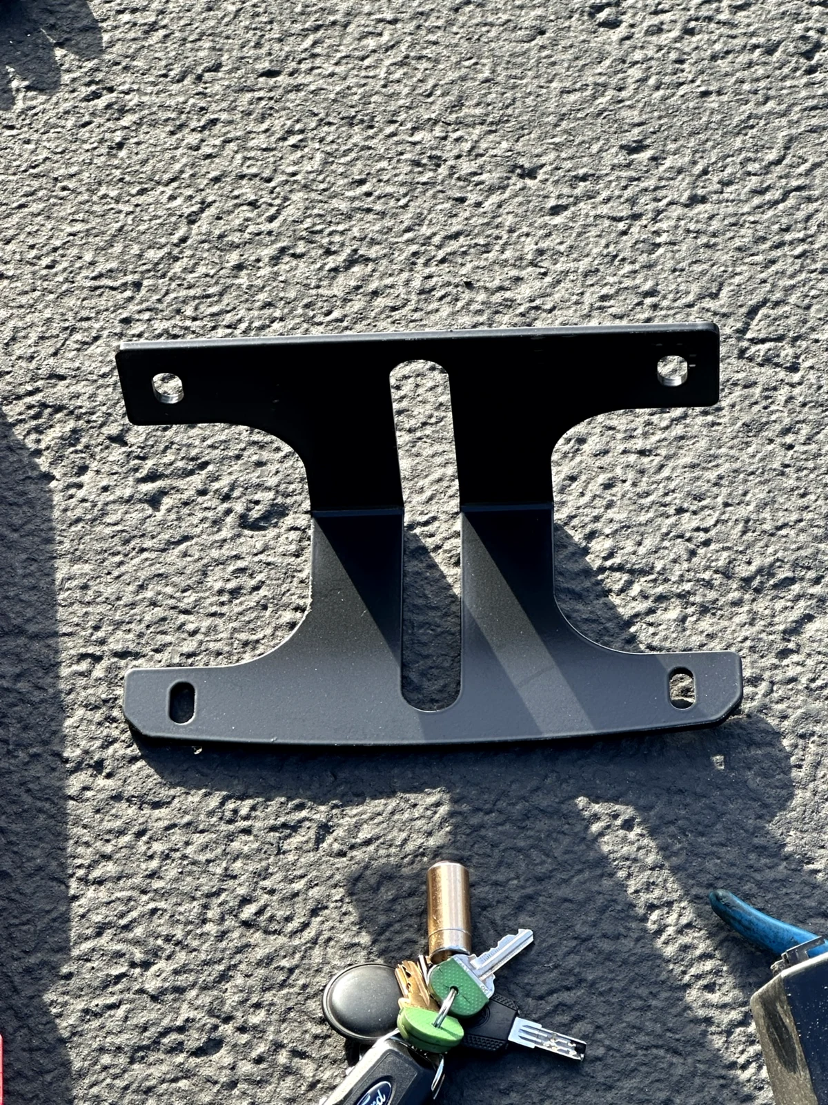 Loose black offset center-support bracket with round and slotted openings on asphalt