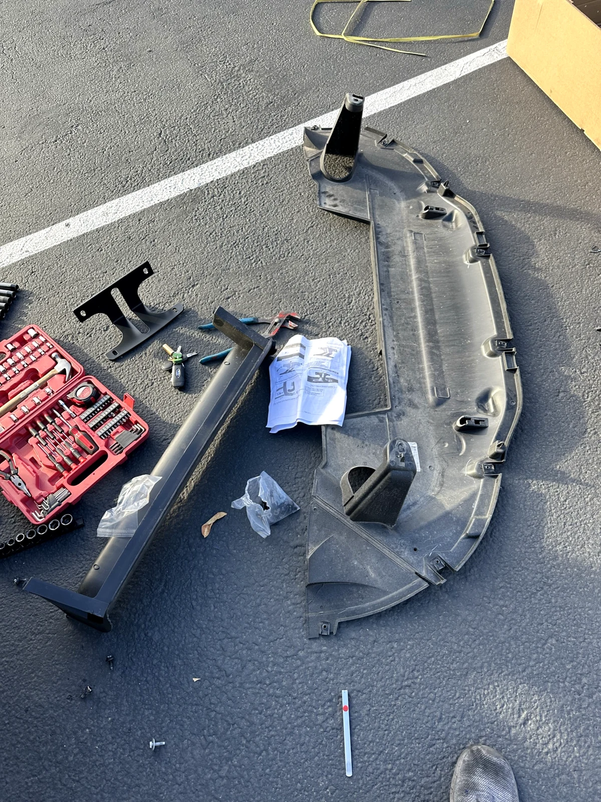 Removed black splash guard on asphalt beside brackets, instructions and tools