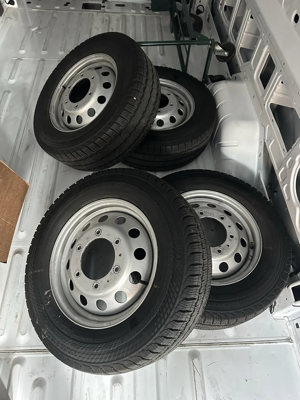 Four removed stock wheel-and-tire assemblies inside the Transit’s bare cargo area.