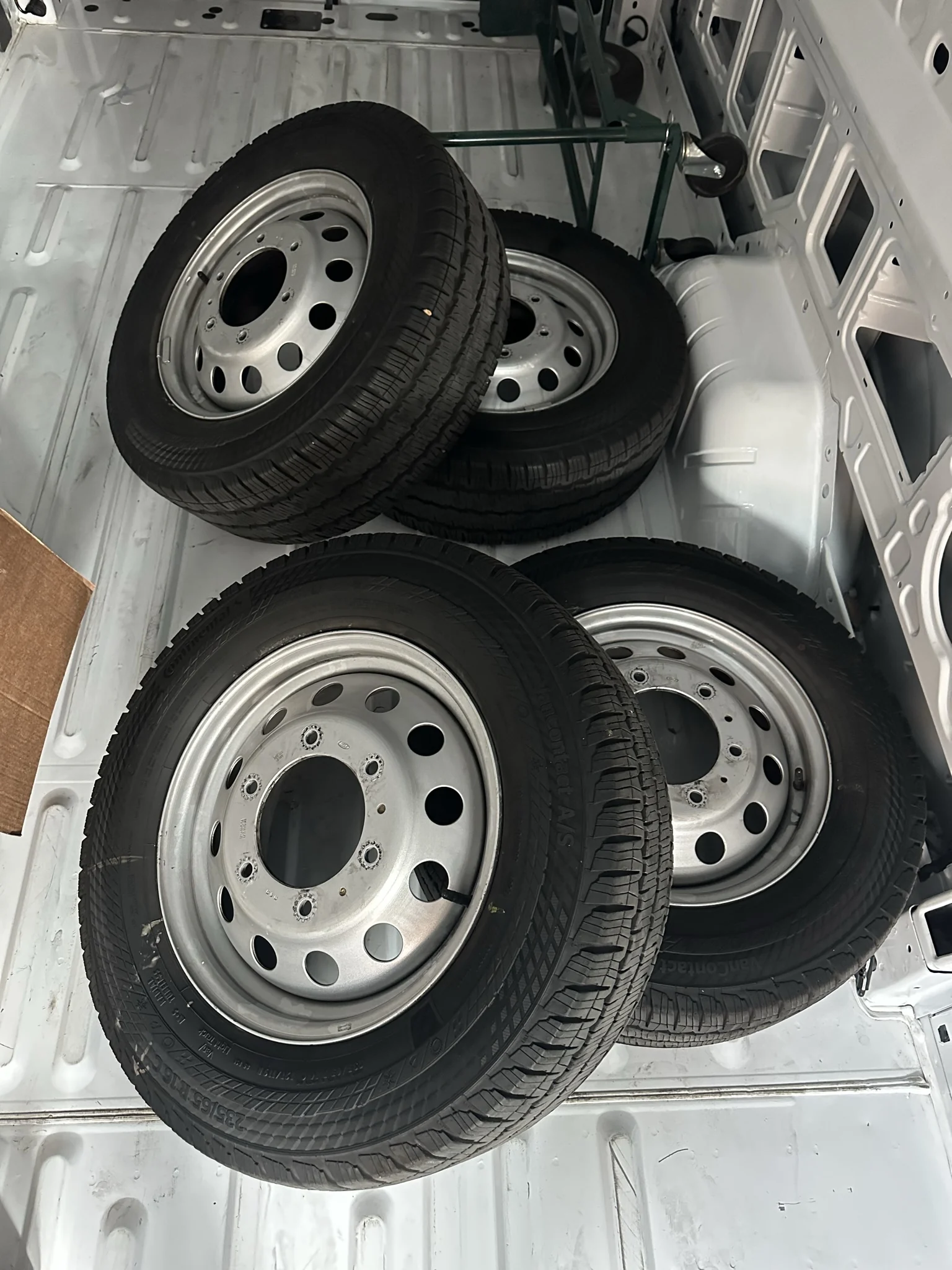 All four removed stock wheel-and-tire assemblies in the cargo area.