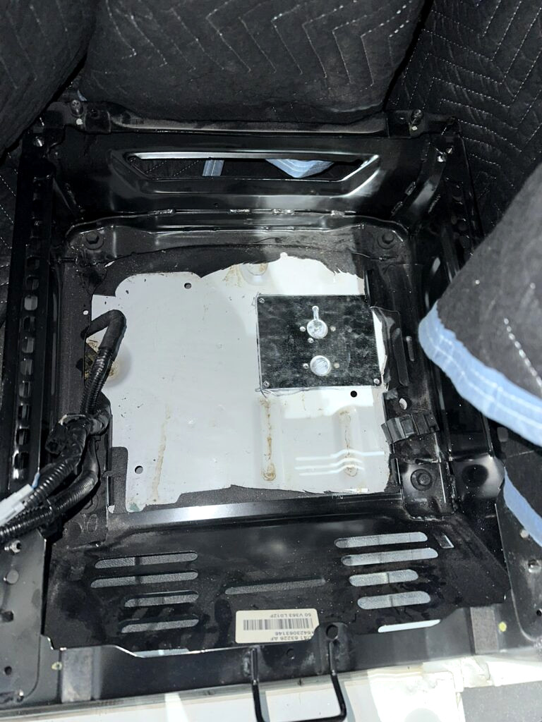 Mounting plate beside the marked floor opening under the passenger seat.